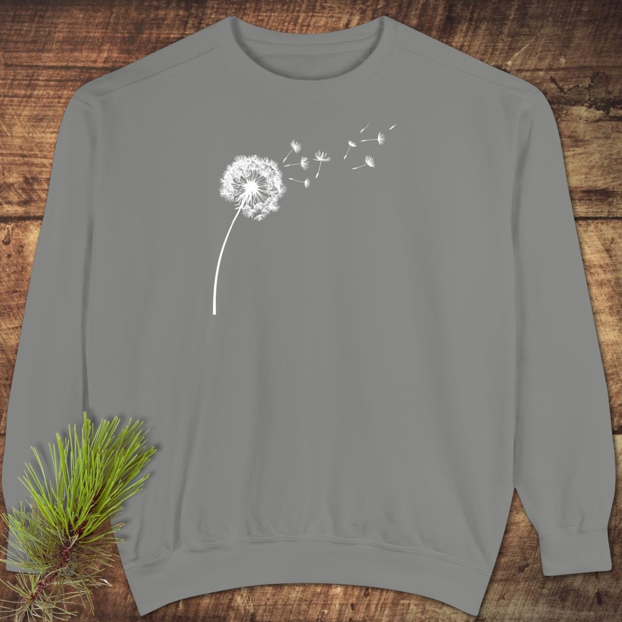 Dandelion Comfort Colors Sweatshirt on wooden surface, featuring a white dandelion print. Made of 80% cotton, 20% polyester, relaxed fit.