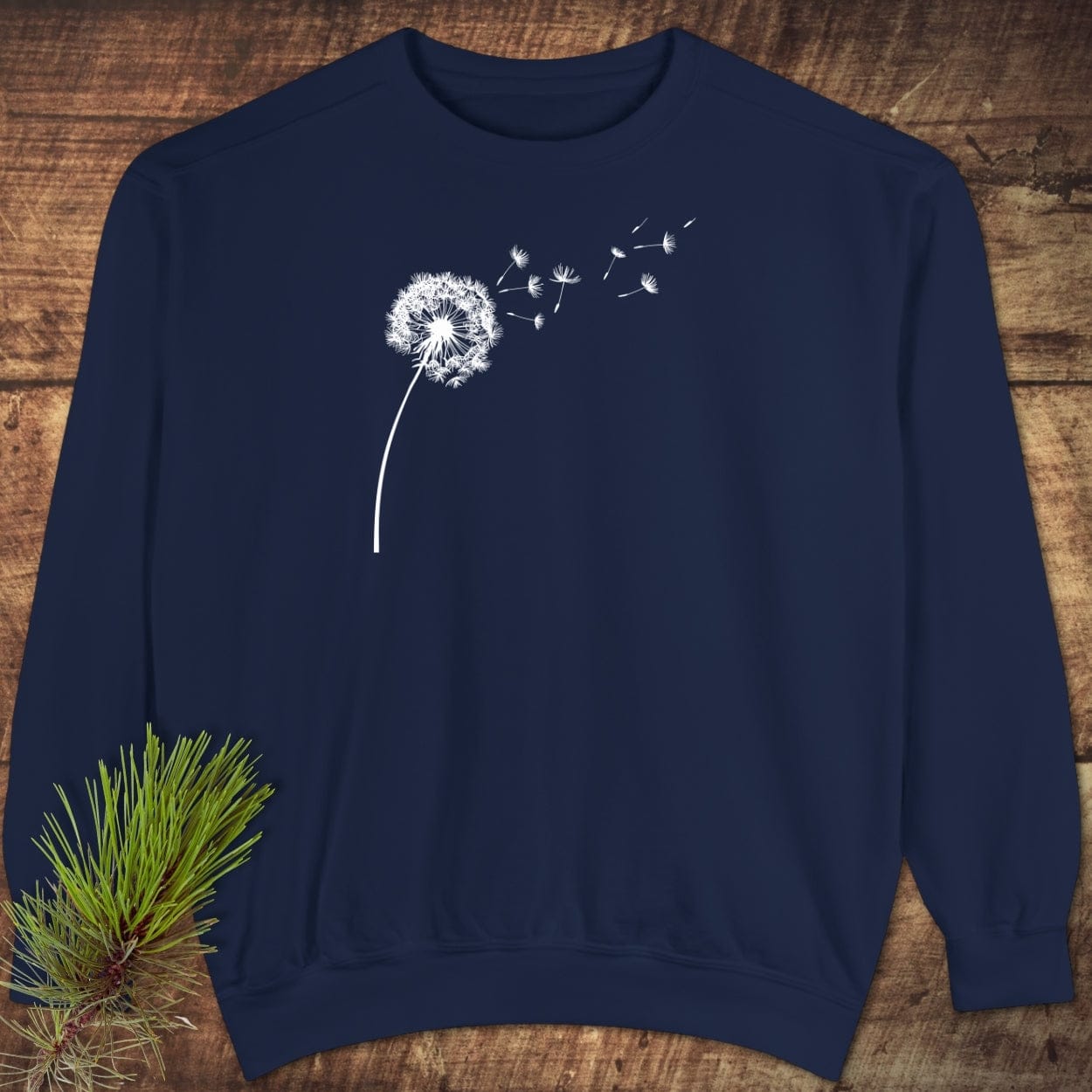 Navy-blue crewneck sweatshirt with a white dandelion graphic, laid flat on wood. Features relaxed fit, rolled-forward shoulder, made of 80% ring-spun cotton.