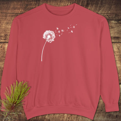 Dandelion Comfort Colors Sweatshirt on wood surface; features white dandelion print, relaxed fit, 80% cotton, 20% polyester. Pine sprig nearby.