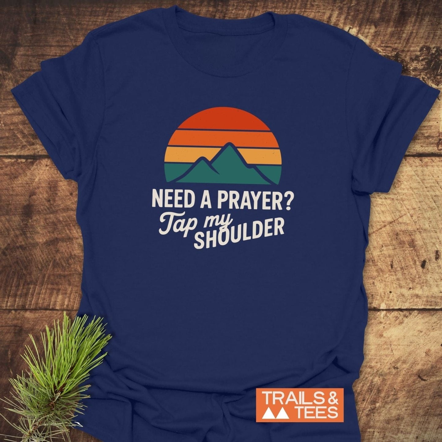 Navy-blue Tap My Shoulder Mountain T-Shirt with retro sun/mountain print, laid on wood. Features soft cotton, durable print, and no side seams.