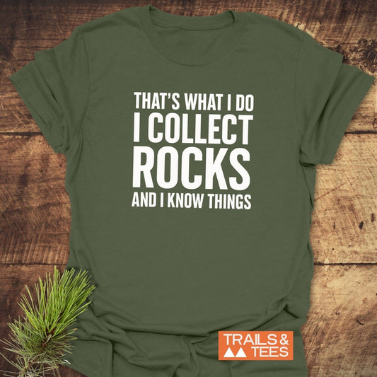 Army-green I Collect Rocks T-shirt with bold white text, orange TRAILS & TEES logo, laid on wood. Made from soft, durable ring-spun cotton.