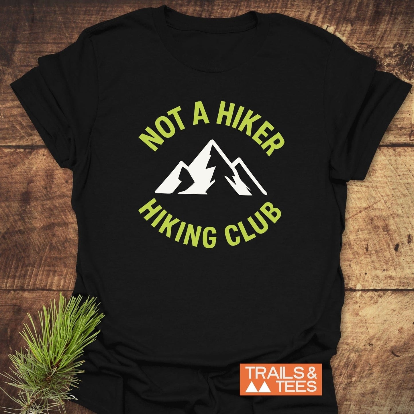 Not A Hiker T-Shirt featuring a mountain graphic and text, laid on wood. Crafted from soft cotton, ensuring comfort and durability with eco-friendly production.