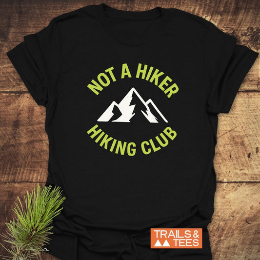 Not A Hiker T-Shirt featuring a mountain graphic and text, laid on wood. Crafted from soft cotton, ensuring comfort and durability with eco-friendly production.