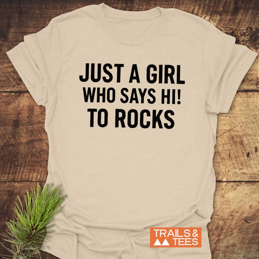 Say Hi To Rocks T-Shirt on rustic wood, featuring bold black text. Made from soft, durable ring-spun cotton, perfect for outdoor enthusiasts.