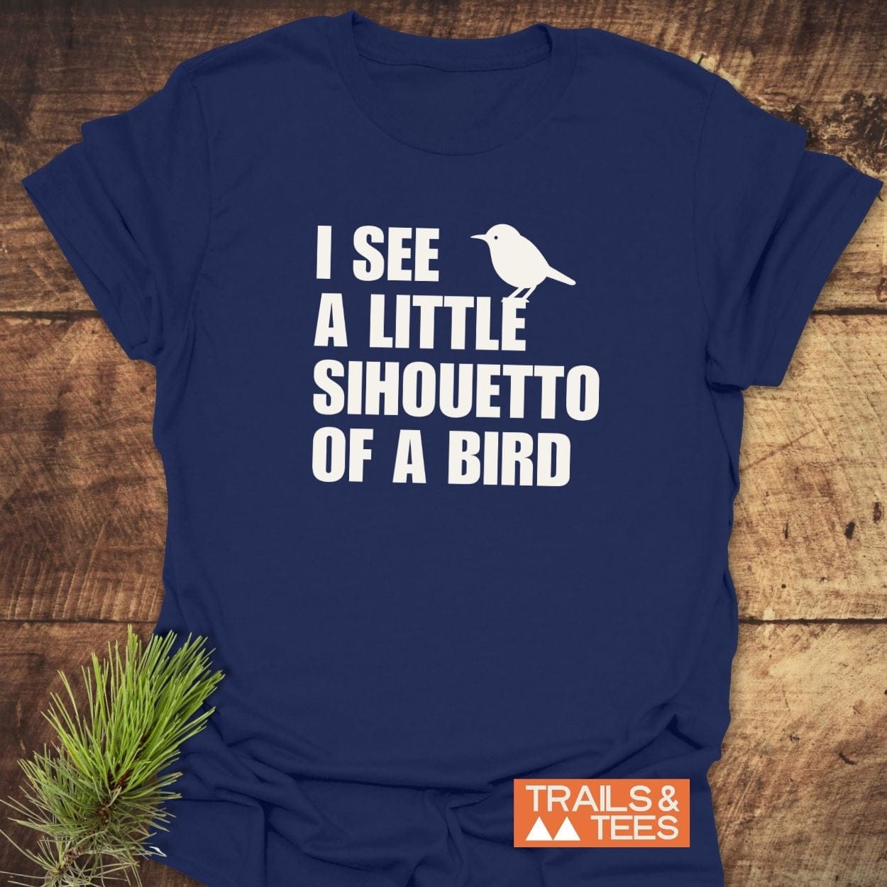 Silhouetto Of A Bird Funny T-Shirt with bold white text and bird silhouette, featuring TRAILS & TEES logo, styled with a pine sprig.