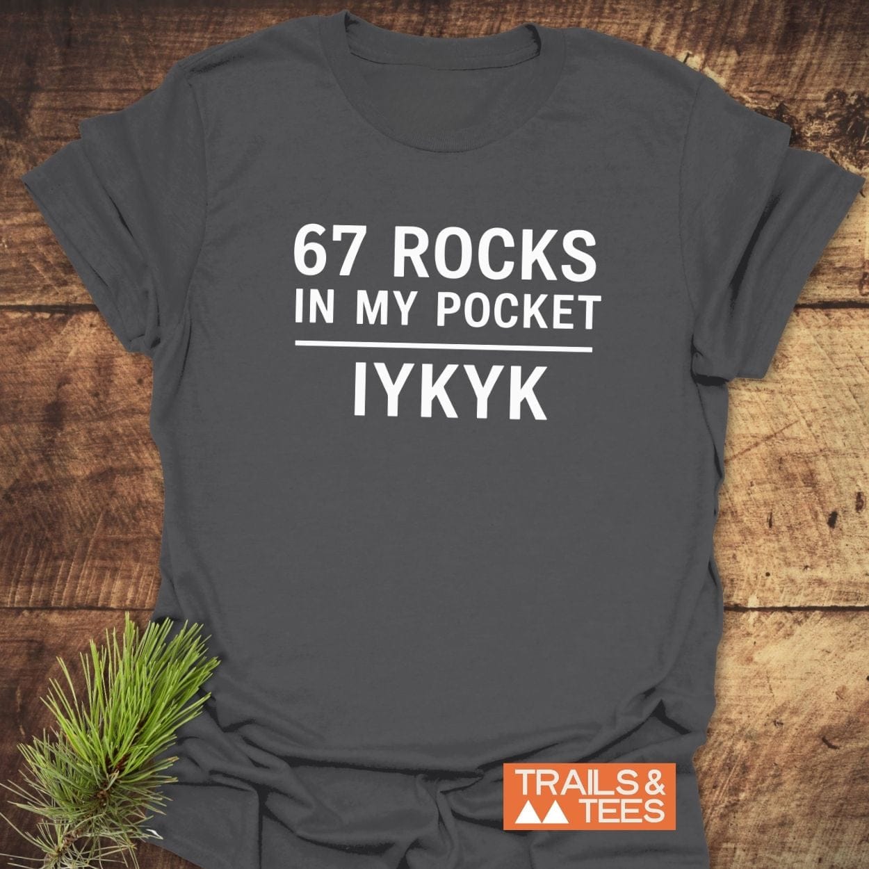 Heather-charcoal T-shirt with white 67 ROCKS IN MY POCKET text, featuring TRAILS & TEES logo, crafted for outdoor comfort and adventure.