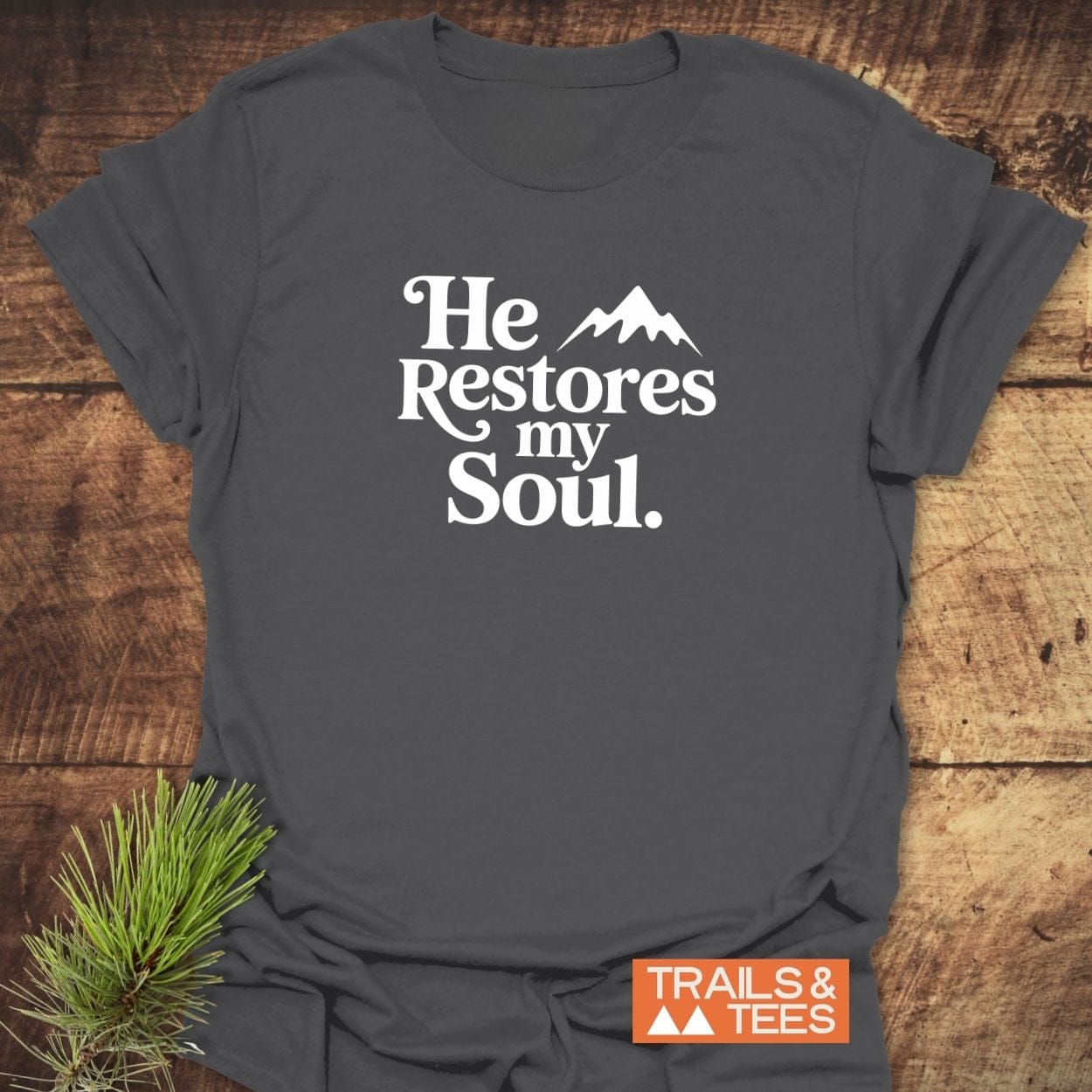He Restores My Soul T-Shirt on wood surface, featuring a white mountain graphic. Made from soft ring-spun cotton with durable print, ideal for outdoor enthusiasts.