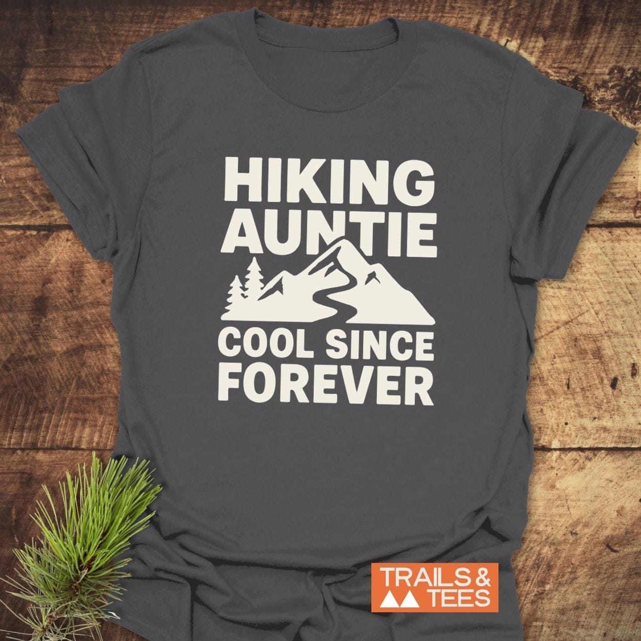 Dark-gray Hiking Auntie T-shirt featuring a mountain scene, crafted from soft cotton, with durable prints and a small Trails & Tees logo.