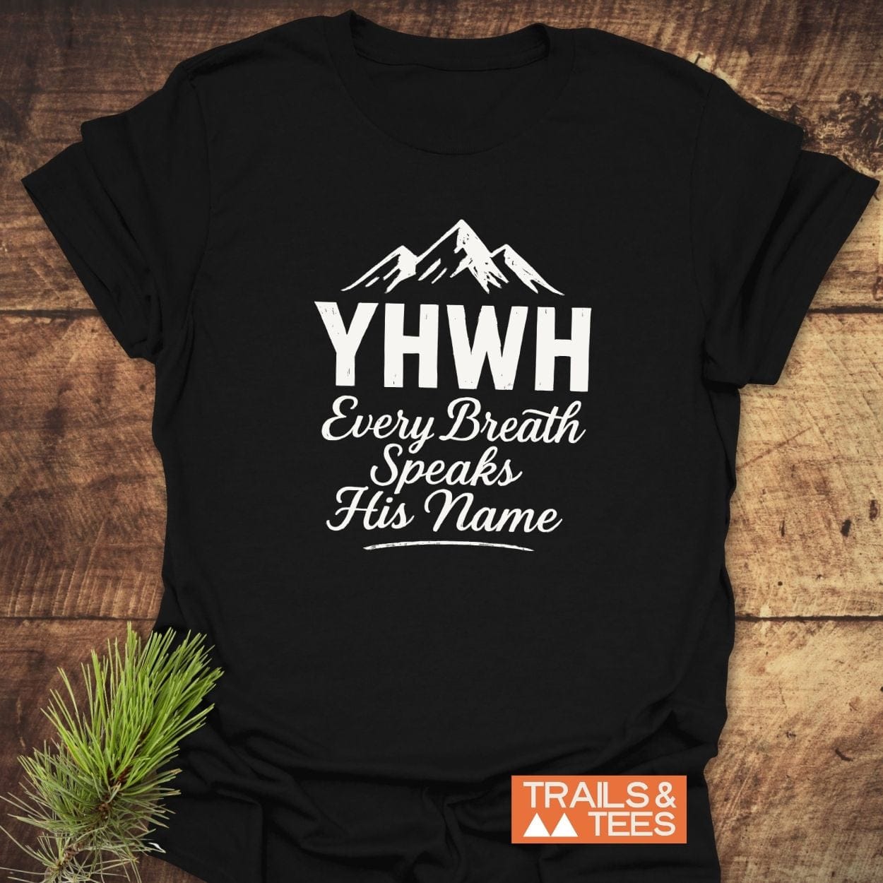 Black T-shirt with mountain graphic and YHWH text, featuring Every Breath Speaks His Name. Includes TRAILS & TEES label. Made from soft, lightweight cotton.