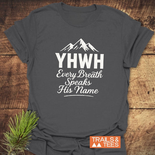 Charcoal T-shirt with YHWH and mountain graphic; Every Breath Speaks His Name. Styled with pine sprig. Made from soft, lightweight cotton for outdoor enthusiasts.