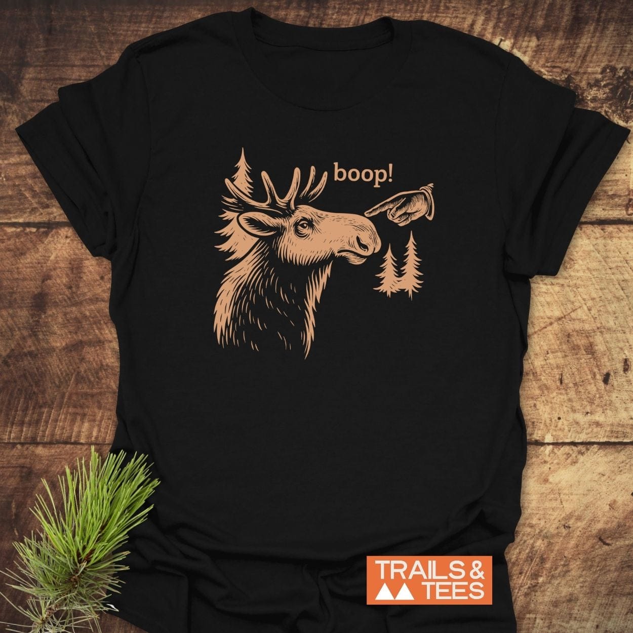 BOOP Moose Funny T-Shirt featuring a moose sketch with boop! graphic, surrounded by pine trees, on soft ring-spun cotton, captured on wooden surface.