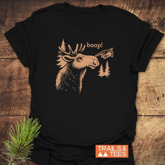 BOOP Moose Funny T-Shirt featuring a moose sketch with boop! graphic, surrounded by pine trees, on soft ring-spun cotton, captured on wooden surface.