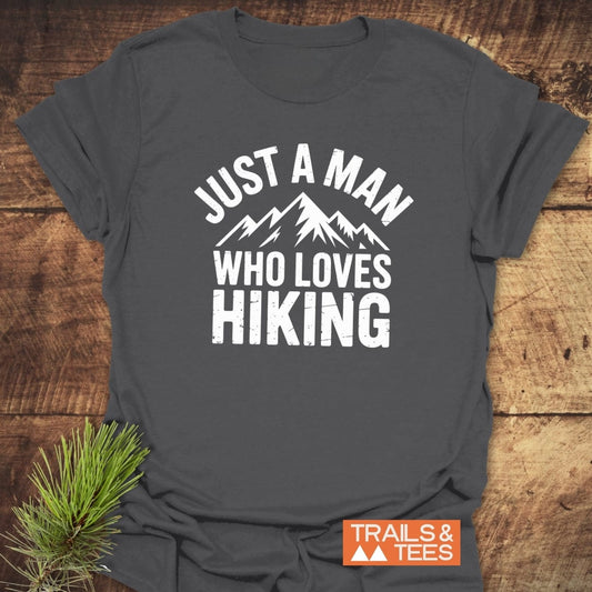 Charcoal-gray T-shirt with white stylized mountain peaks and JUST A MAN WHO LOVES HIKING text, emphasizing outdoor passion and adventure.