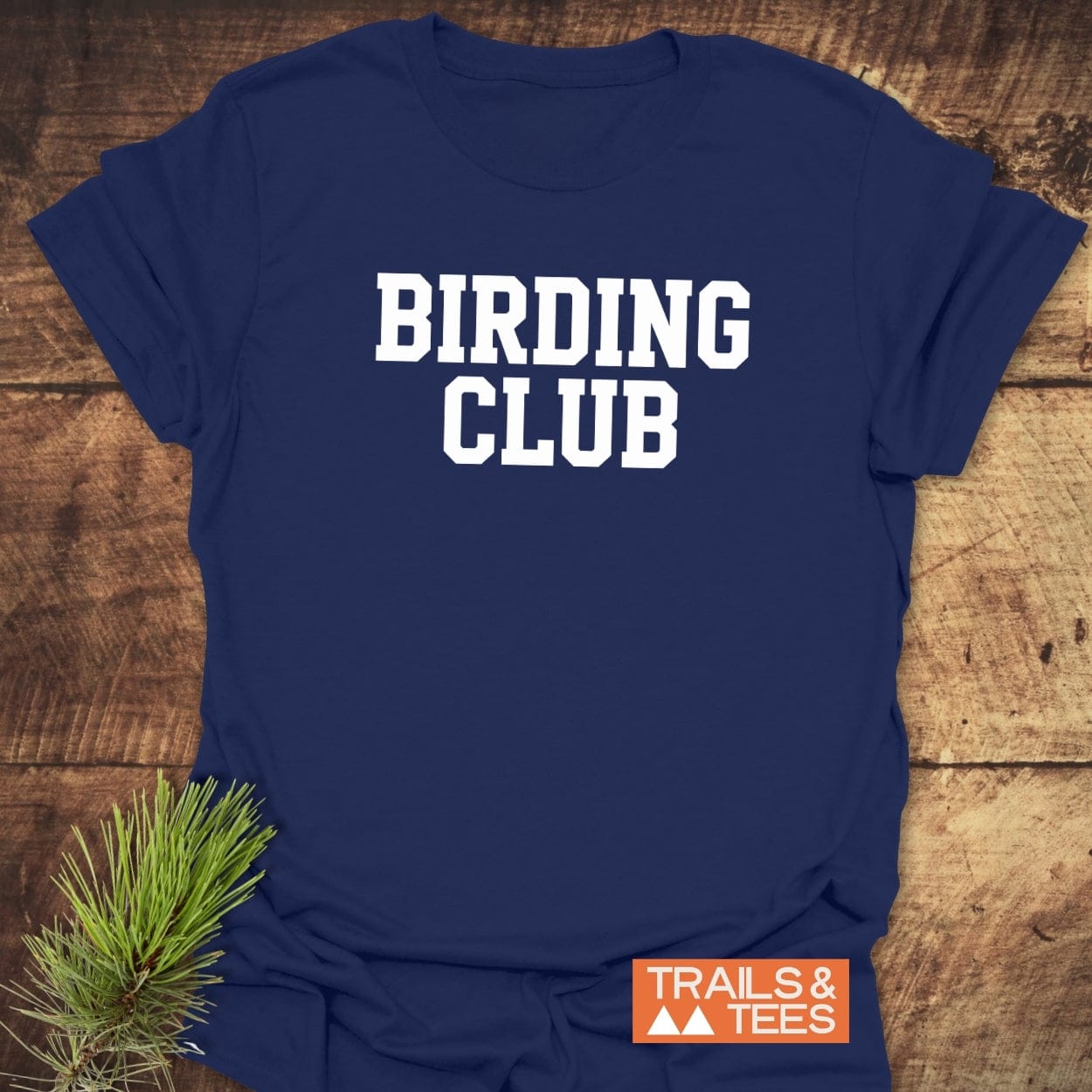Birding Club T-Shirt on rustic wood, featuring bold white lettering and TRAILS & TEES logo, highlighting comfort and adventure-ready design.