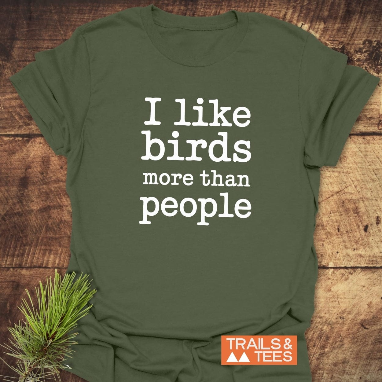 Olive-green T-shirt with I Like Birds More Than People slogan, showcasing TRAILS & TEES logo, highlighting comfort and durability with pre-shrunk, soft ring-spun cotton.