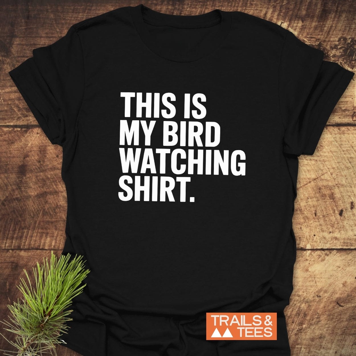 Bird Watching T-Shirt with bold white lettering, THIS IS MY BIRD WATCHING SHIRT, featuring the Trails & Tees logo, laid on a wooden surface.