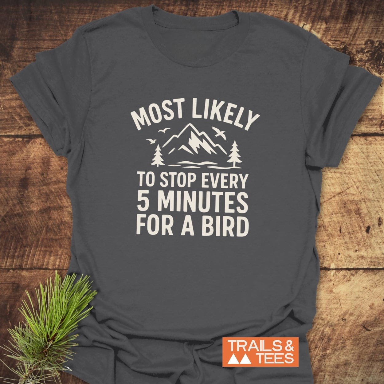 Most Likely Bird Watcher T-Shirt with mountain-and-tree graphic, birds, and humorous text on charcoal-gray cotton, showcasing outdoor adventure spirit.