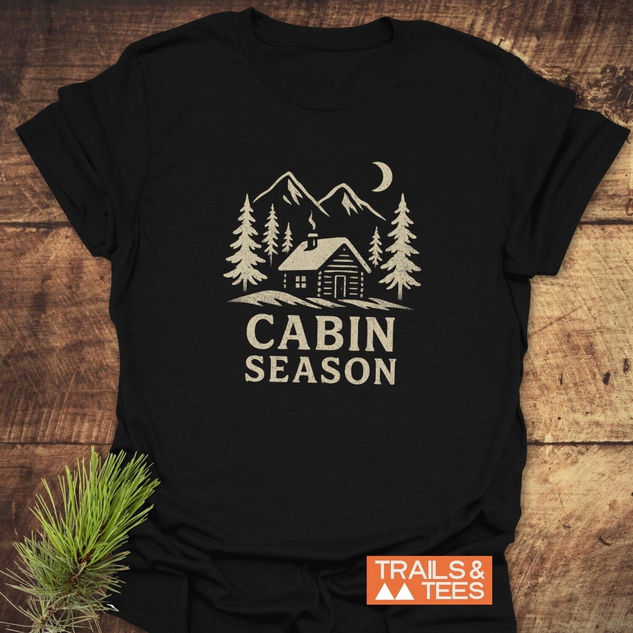 Cabin Season T-Shirt featuring a log cabin graphic among pine trees and mountains, crafted from soft cotton for comfort, ideal for outdoor enthusiasts.
