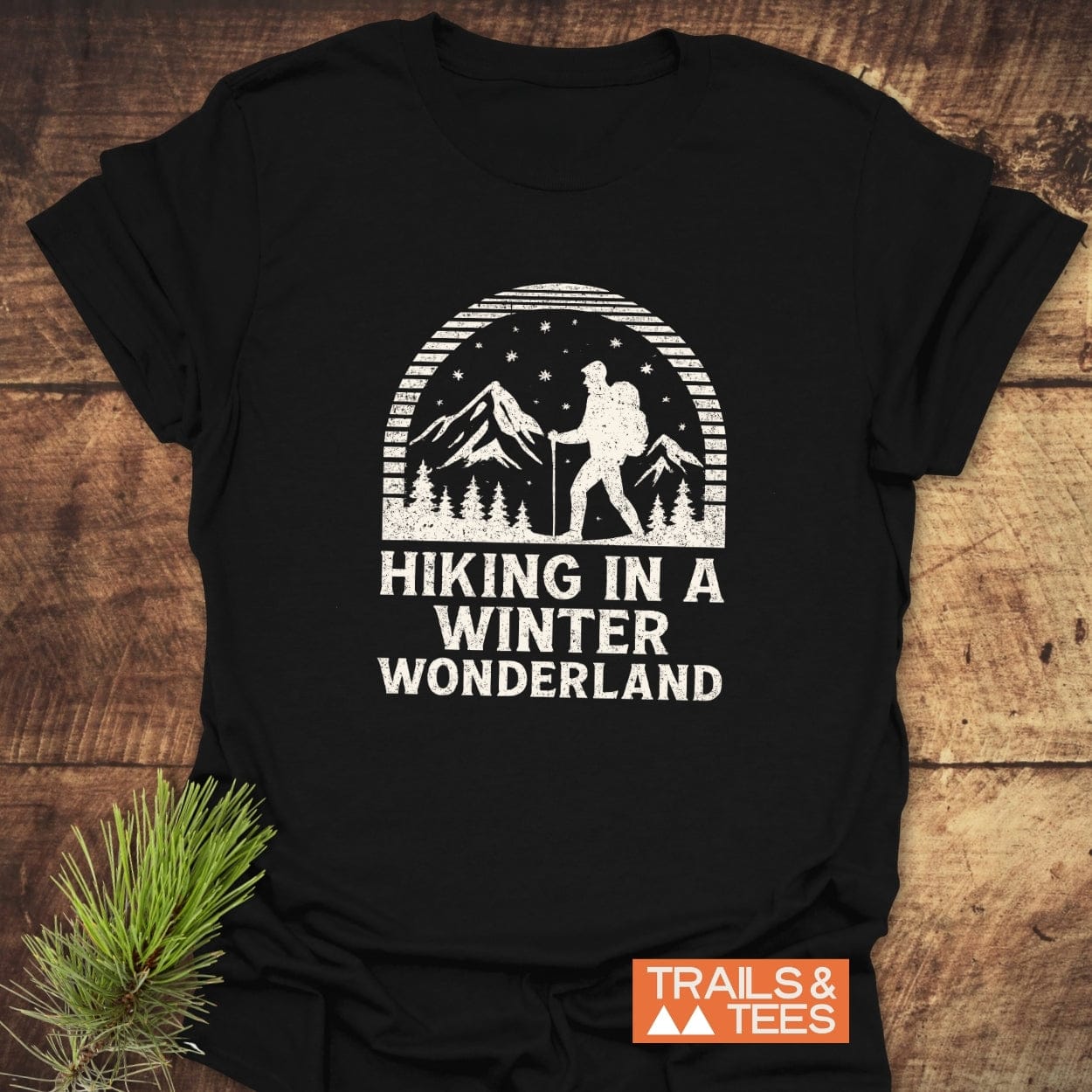 Hiking In A Winter Wonderland T-Shirt: Black tee with a distressed graphic of a hiker, pine trees, and mountains. Features comfort-focused, durable design by Trails & Tees.