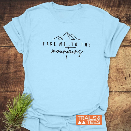 Take Me To The Mountains Minimal T-Shirt with mountain line-drawing, black text; soft ring-spun cotton, pre-shrunk, durable print, beside TRAILS & TEES logo and pine sprig.