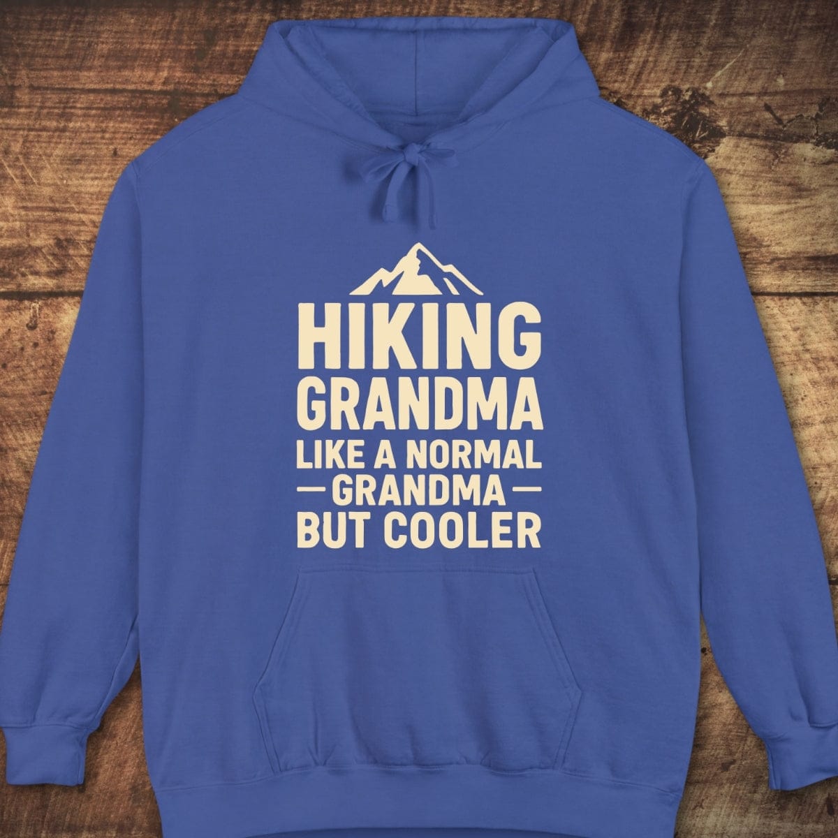 Hiking Grandma Comfort Colors Hoodie features a stylized mountain graphic with playful text, royal-blue hue, kangaroo pocket, and relaxed fit for trail comfort.