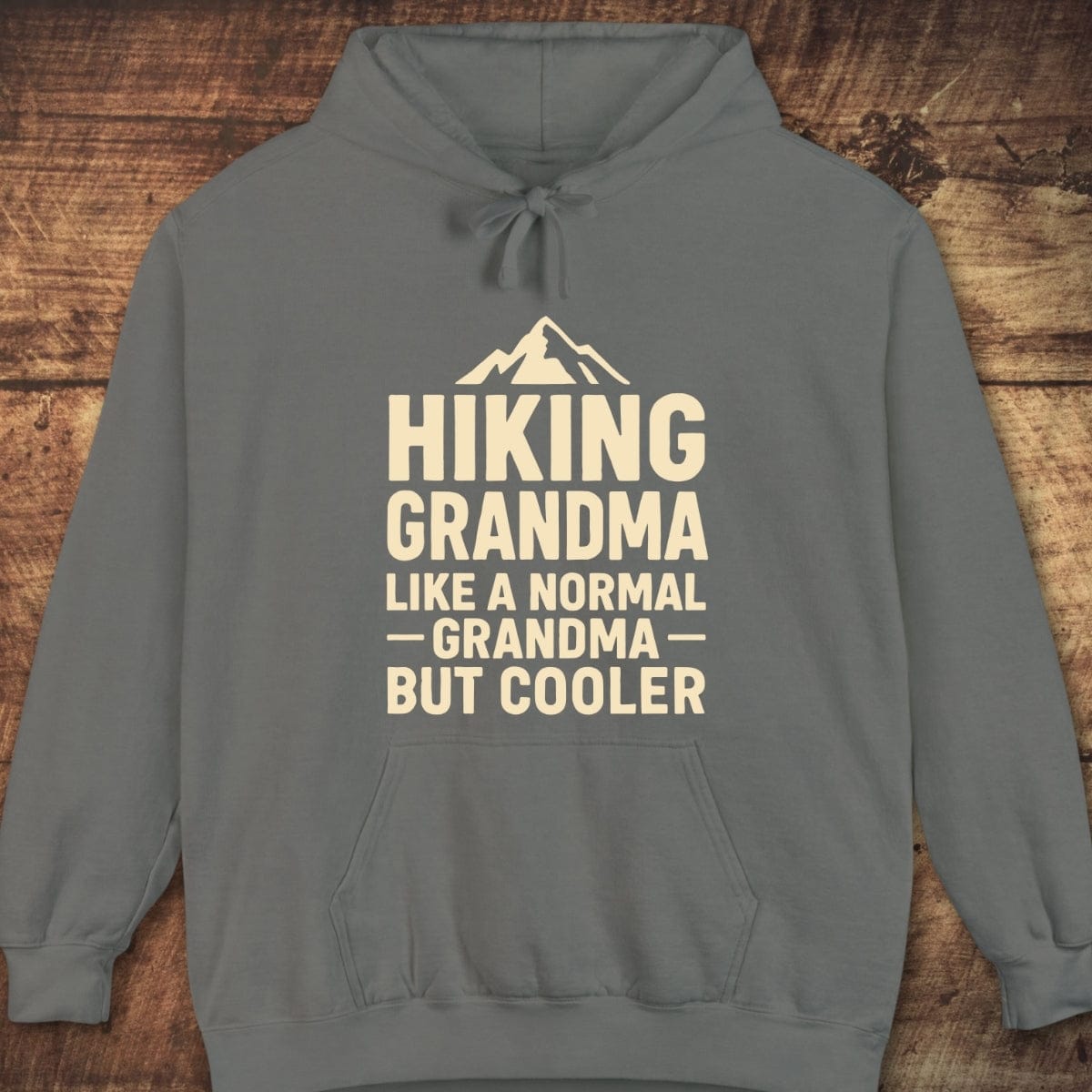 Gray pullover hoodie with cream mountain graphic and text Hiking Grandma, Like a Normal Grandma But Cooler, showcasing a relaxed fit and cozy, trail-ready design.