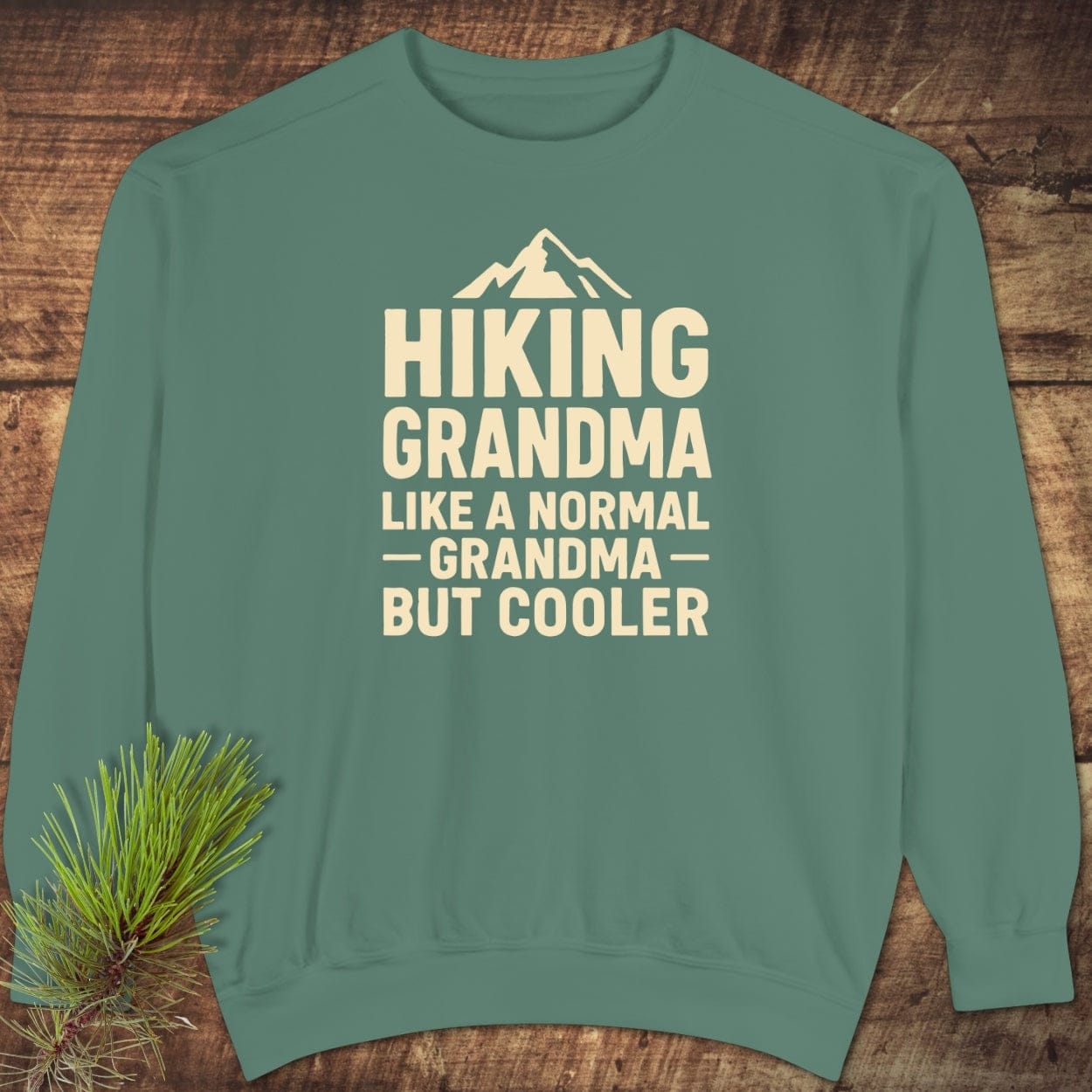 Hiking Grandma Comfort Colors Sweatshirt: Teal-green crewneck with cream lettering and mountain icon, highlighting HIKING GRANDMA text. Relaxed fit, garment-dyed fleece for luxurious comfort.
