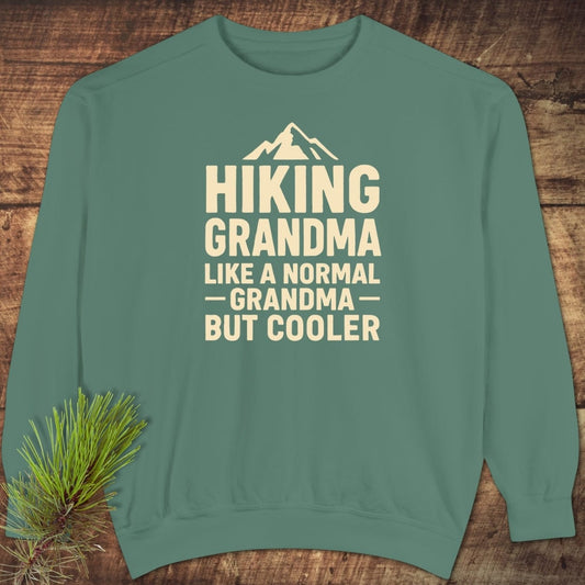 Hiking Grandma Comfort Colors Sweatshirt: Teal-green crewneck with cream lettering and mountain icon, highlighting HIKING GRANDMA text. Relaxed fit, garment-dyed fleece for luxurious comfort.