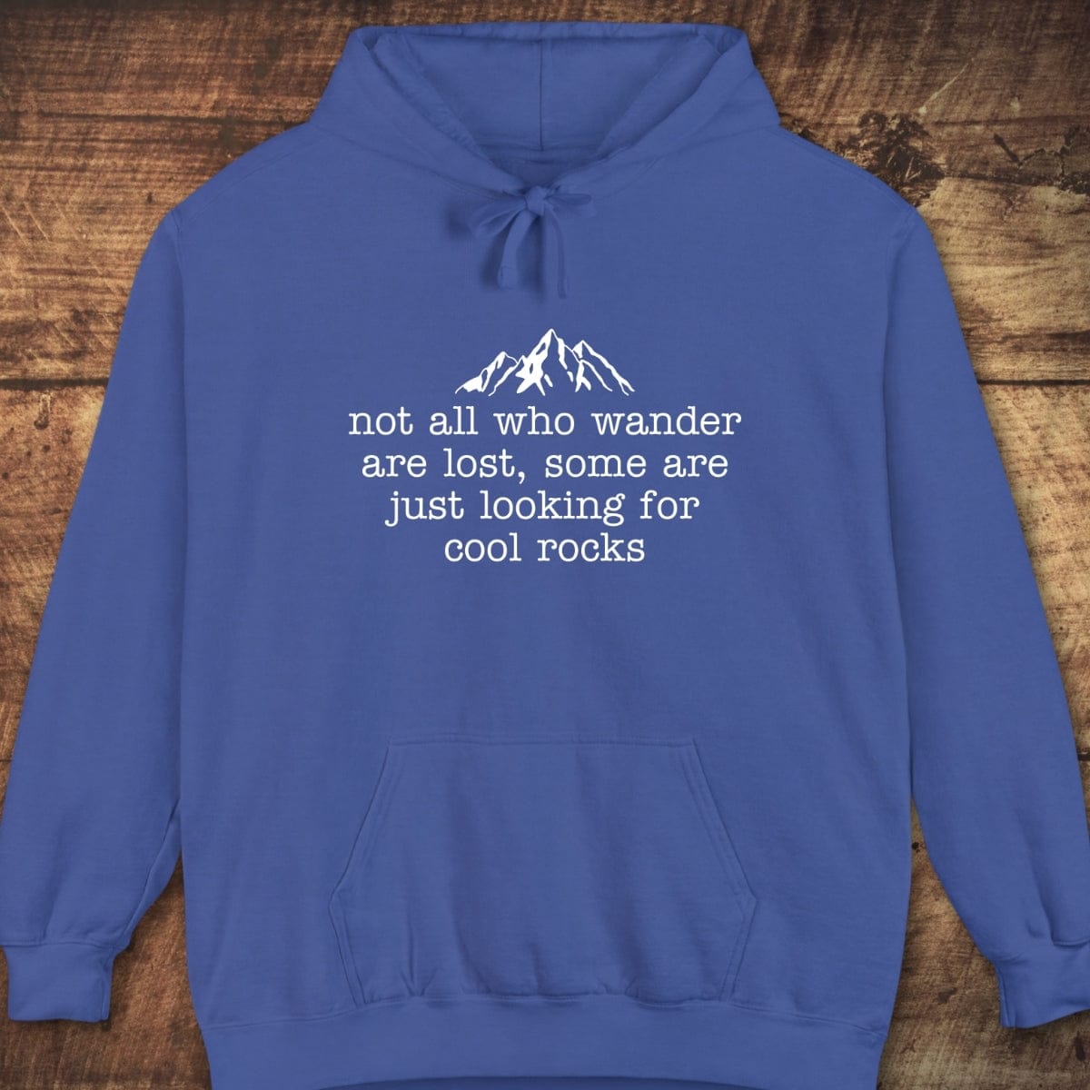 Looking For Cool Rocks Comfort Colors Hoodie with mountain graphic and text, featuring a relaxed fit, jersey-lined hood, and front pouch pocket on wooden background.