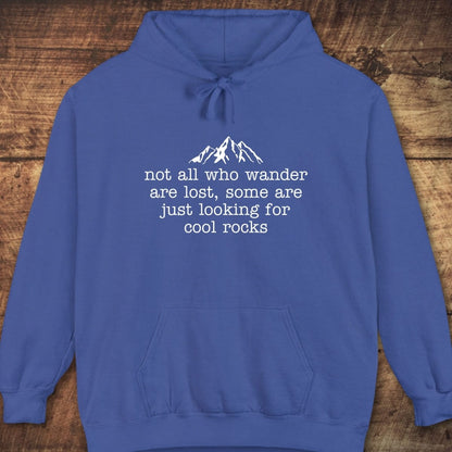 Looking For Cool Rocks Comfort Colors Hoodie with mountain graphic and text, featuring a relaxed fit, jersey-lined hood, and front pouch pocket on wooden background.