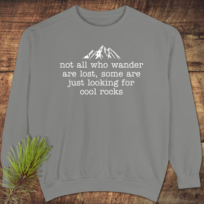 Looking For Cool Rocks Comfort Colors Sweatshirt, featuring a mountain graphic and quote, laid flat with a pine sprig, showcasing its relaxed fit and luxurious fabric.