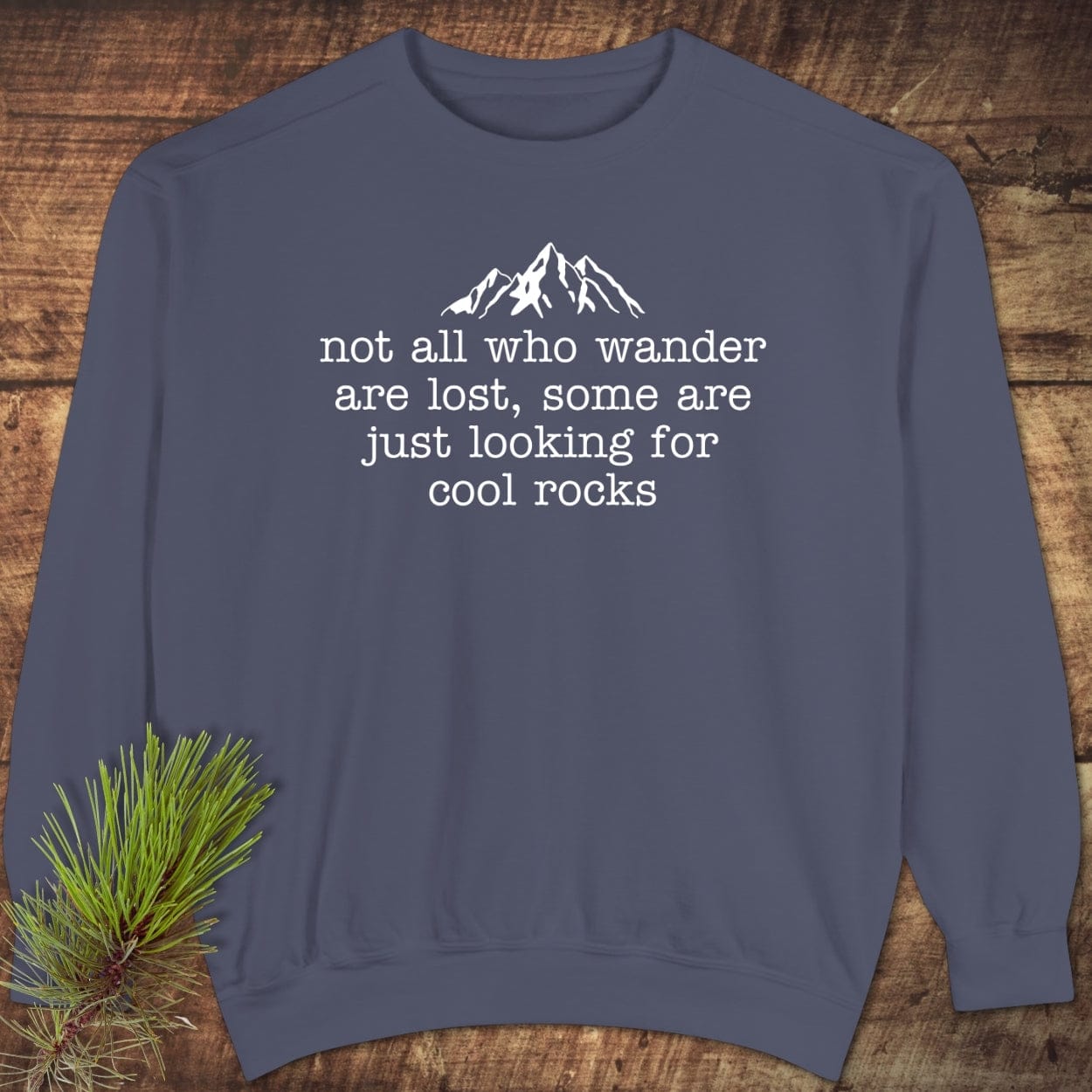 Looking For Cool Rocks Comfort Colors Sweatshirt with mountain graphic and quote, laid on wood. Features relaxed fit, garment-dyed fabric, and ring-spun cotton blend.