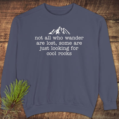 Looking For Cool Rocks Comfort Colors Sweatshirt with mountain graphic and quote, laid on wood. Features relaxed fit, garment-dyed fabric, and ring-spun cotton blend.