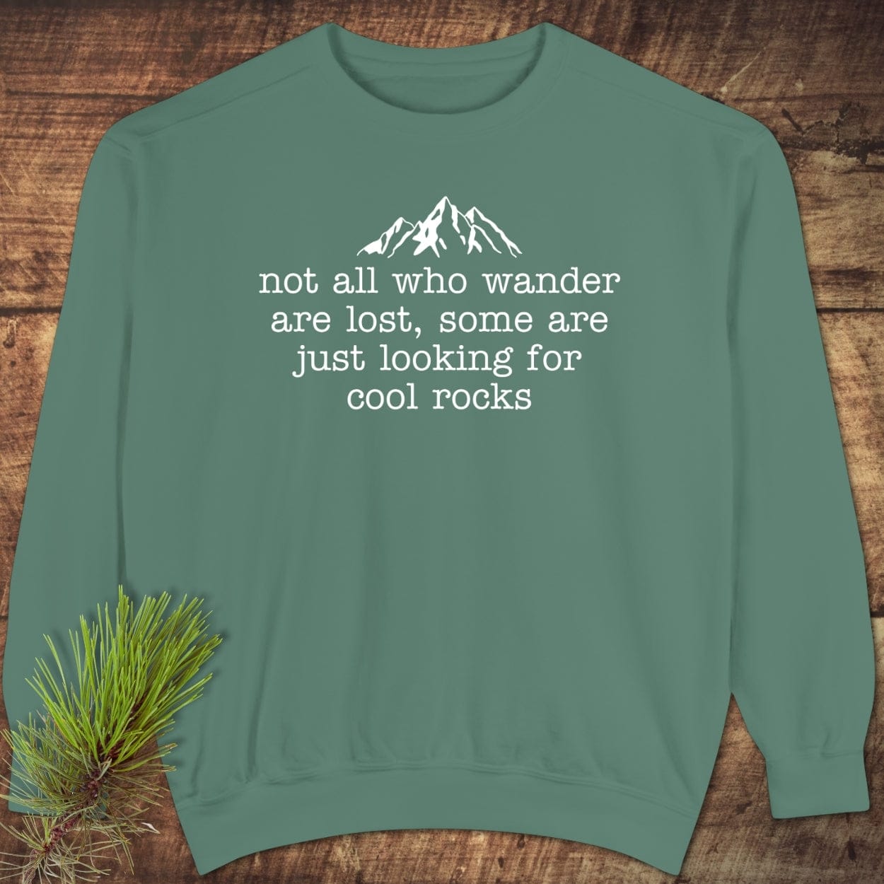 Looking For Cool Rocks Comfort Colors Sweatshirt: Sage-green with a mountain graphic and text, styled with evergreen sprig, showcasing relaxed fit and garment-dyed fabric.
