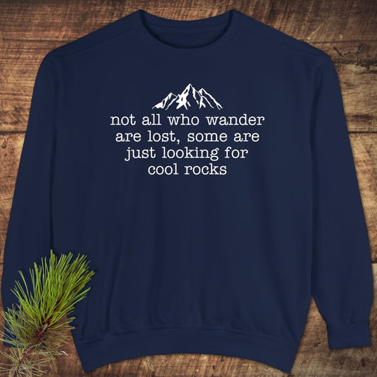 Navy-blue crewneck sweatshirt with mountain graphic and not all who wander quote, styled on wood. Featuring relaxed fit and luxurious, garment-dyed fabric.