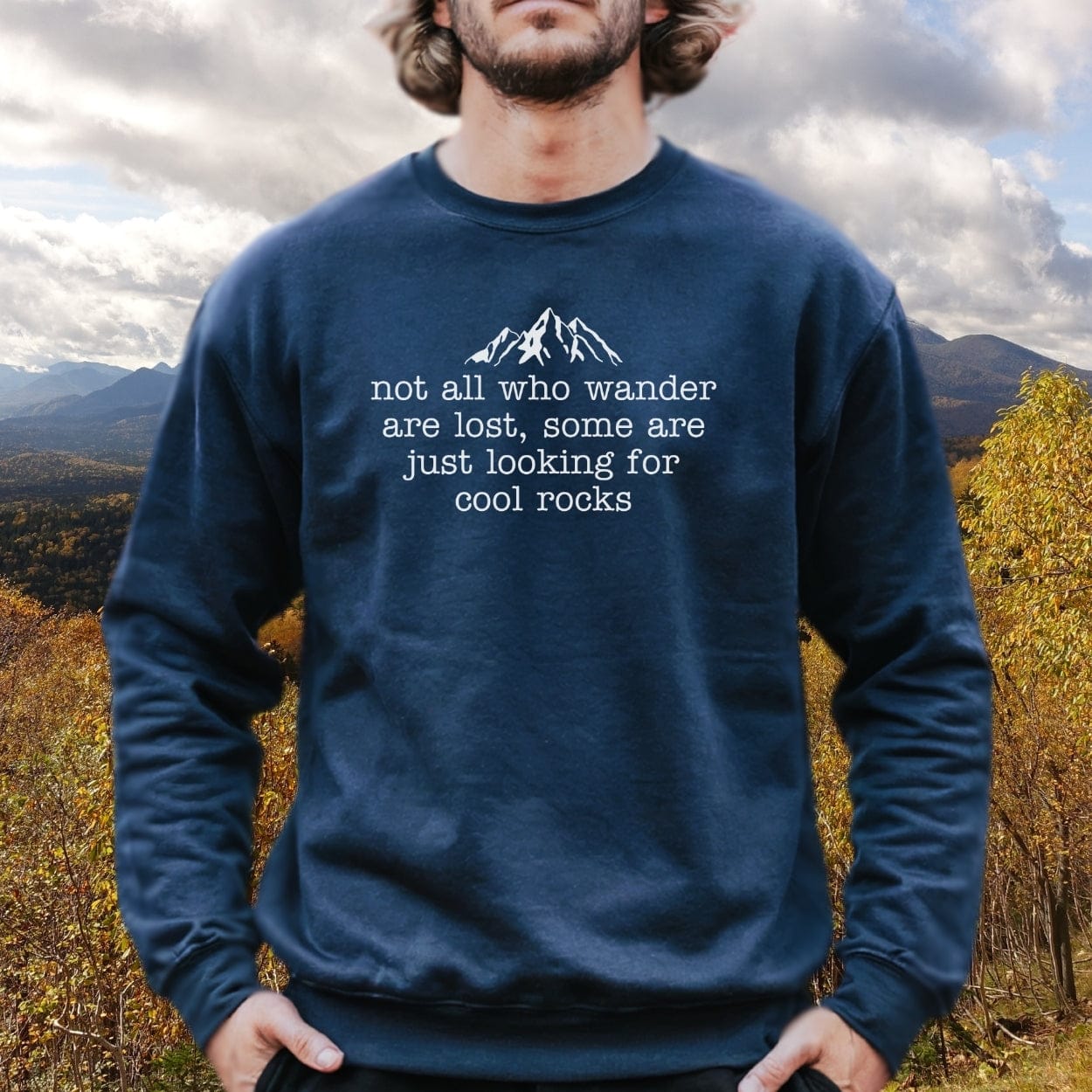 Person in mountainous landscape wearing Looking For Cool Rocks Comfort Colors Sweatshirt, featuring a white mountain line-drawing and quote, showcasing a relaxed fit and rolled-forward shoulder.