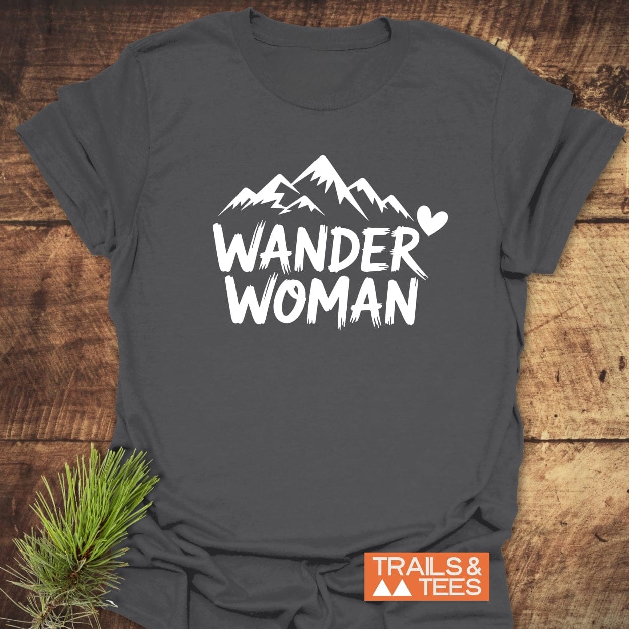 Wander Woman T-Shirt with mountain design in white, laid flat, showcasing soft, lightweight cotton ideal for outdoor adventures. Includes Trails & Tees logo.