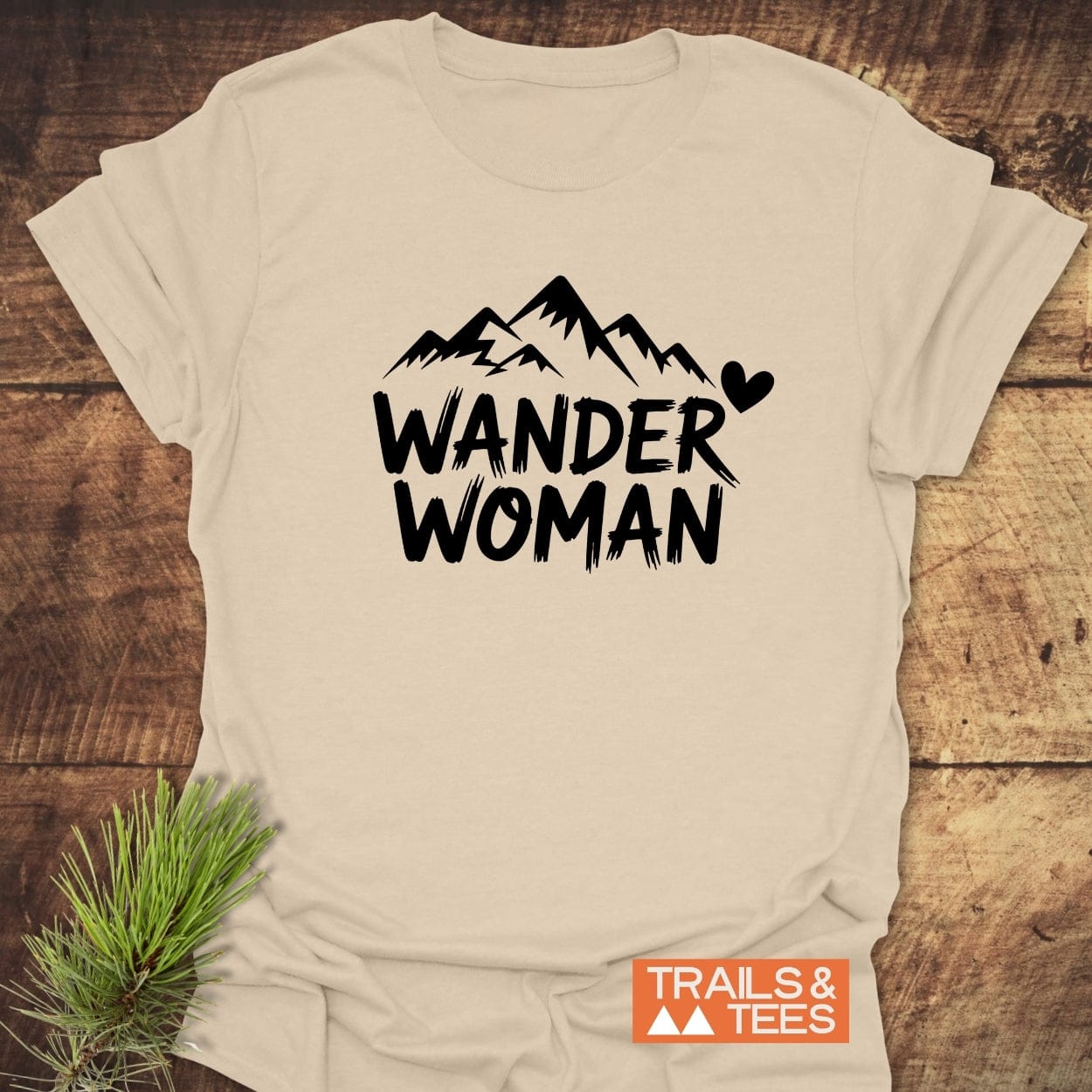 Wander Woman T-Shirt with mountain graphic and heart, crafted from soft ring-spun cotton, offering comfort and durability for outdoor adventures. Features Trails & Tees logo.