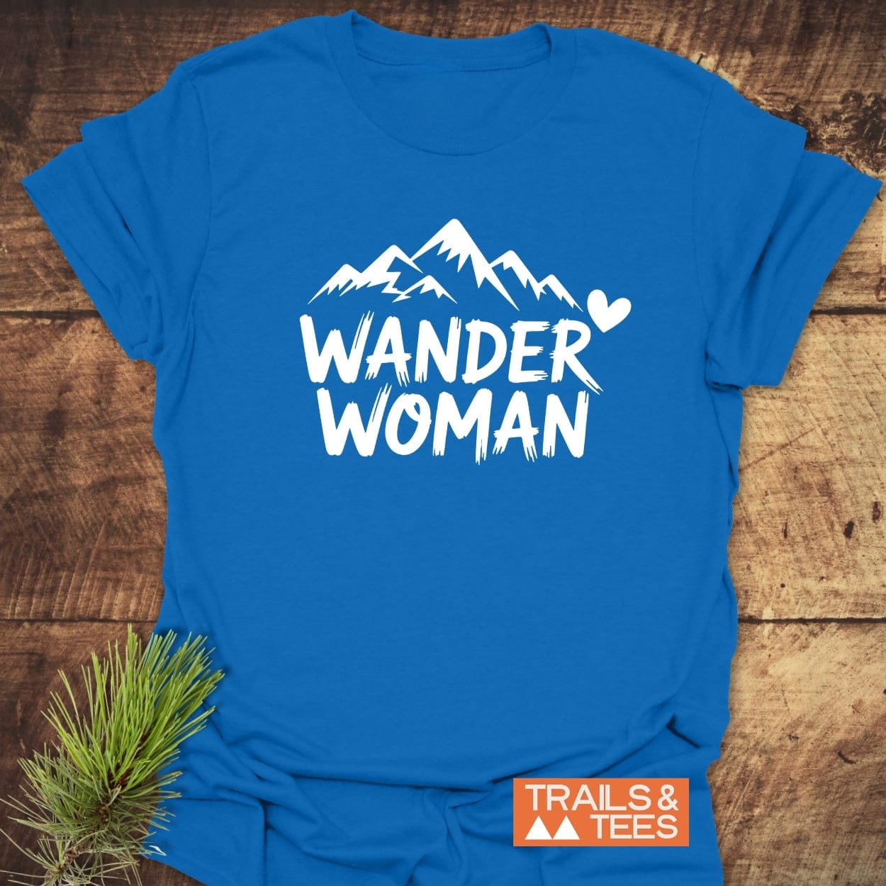Wander Woman T-Shirt featuring mountain graphic and text, laid flat with Trails & Tees label. Soft, durable, pre-shrunk cotton for outdoor adventures.