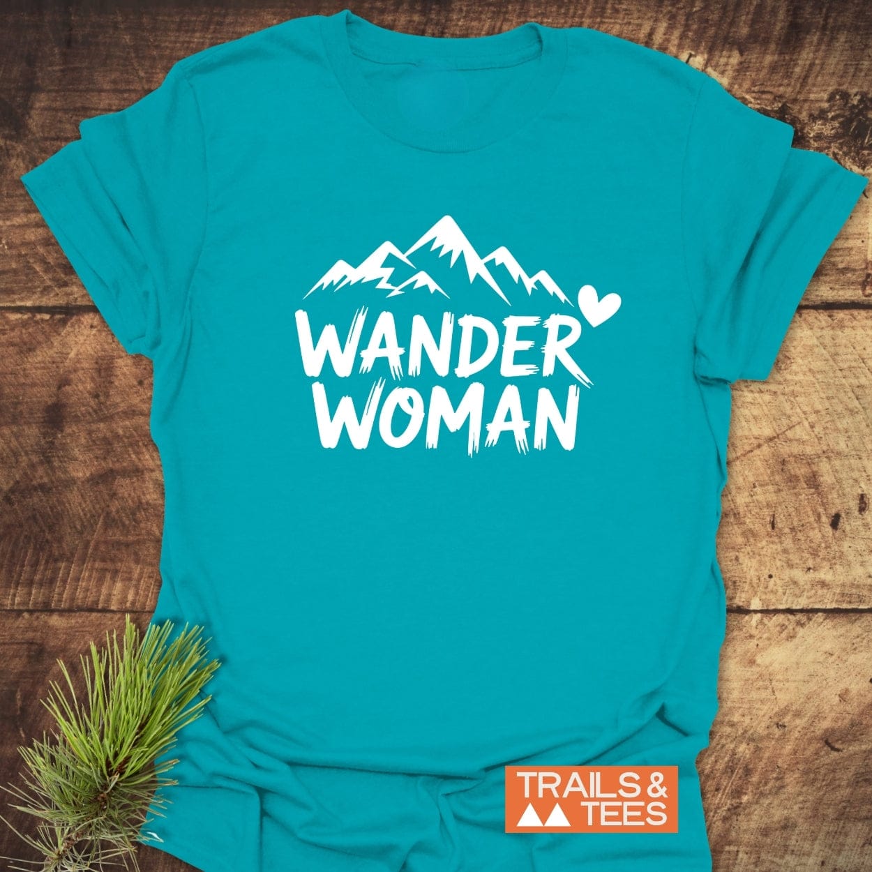 Wander Woman T-Shirt with white mountain peaks graphic and WANDER WOMAN text, featuring durable prints on soft cotton, styled with a pine sprig.