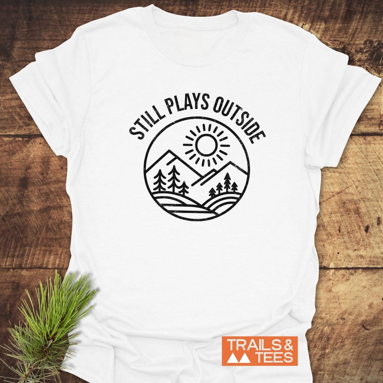 Still Plays Outside T-Shirt featuring a sun, mountains, and trees graphic. Made from soft, lightweight cotton, designed for comfort and durability by Trails & Tees.
