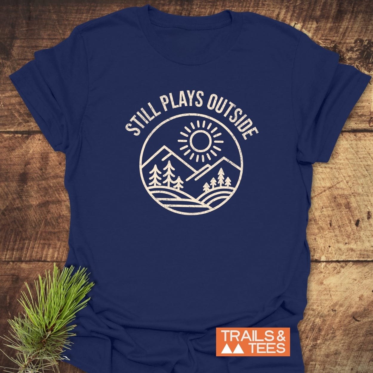 Still Plays Outside T-Shirt with mountain and sun design, crafted from ring-spun cotton, featuring durable prints and a Trails & Tees logo.