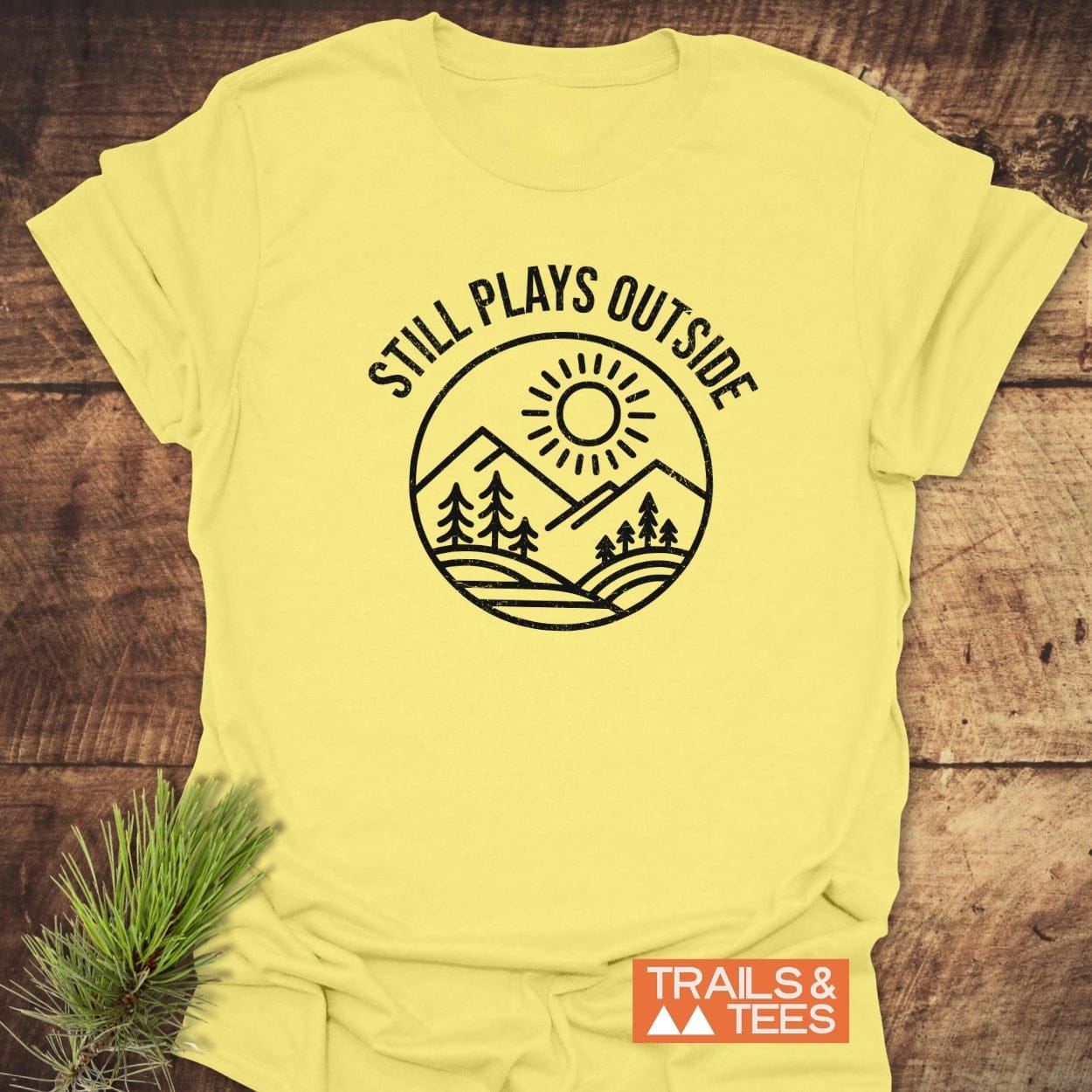 Still Plays Outside T-Shirt featuring a sun, mountains, and trees illustration, crafted from soft cotton for comfort and durability, perfect for outdoor enthusiasts.