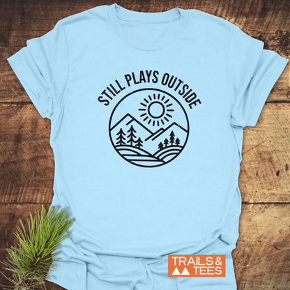 Still Plays Outside T-Shirt featuring a mountain landscape design, crafted from soft ring-spun cotton for comfort and durability, with an orange Trails & Tees label.