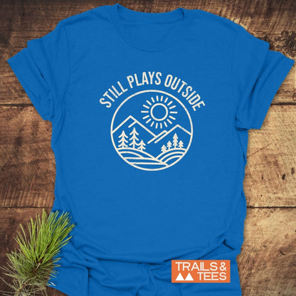 Still Plays Outside T-Shirt featuring a mountain and sun design, crafted from soft cotton, ideal for outdoor enthusiasts, with 'TRAILS & TEES' logo.