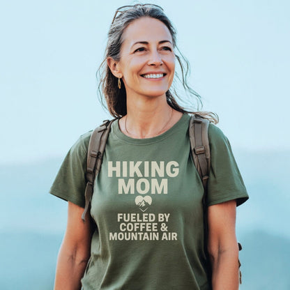 Woman outdoors wearing a Hiking Mom Mountain Air T-Shirt with a daypack; features cream lettering, heart icon, and emphasizes comfort for outdoor adventures.