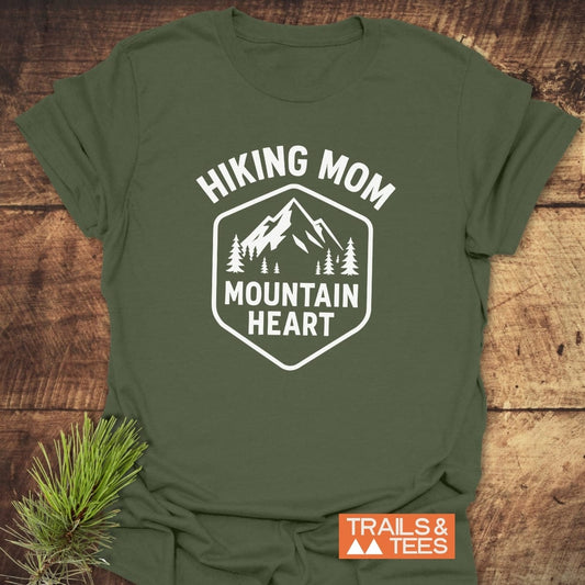 Forest-green Hiking Mom Mountain Heart T-Shirt with mountain badge print, laid on wood. Features soft cotton, durable print, and eco-friendly production.