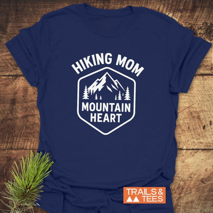 Hiking Mom Mountain Heart T-Shirt displaying a mountain and pine graphic, with HIKING MOM and MOUNTAIN HEART text, laid on wood, featuring a TRAILS & TEES label.