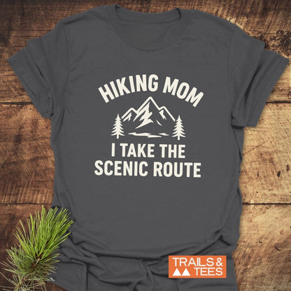 Hiking Mom, Scenic Route T-Shirt with mountain graphic and pine trees, laid flat on wood, embodies comfort and adventure spirit, perfect for outdoor enthusiasts.