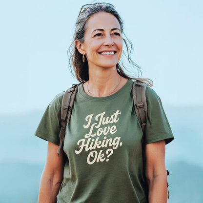 Middle-aged woman outdoors wearing I Just Love Hiking T-shirt, backpack, sunglasses on head; showcasing trail-tested comfort and durable design for outdoor enthusiasts.